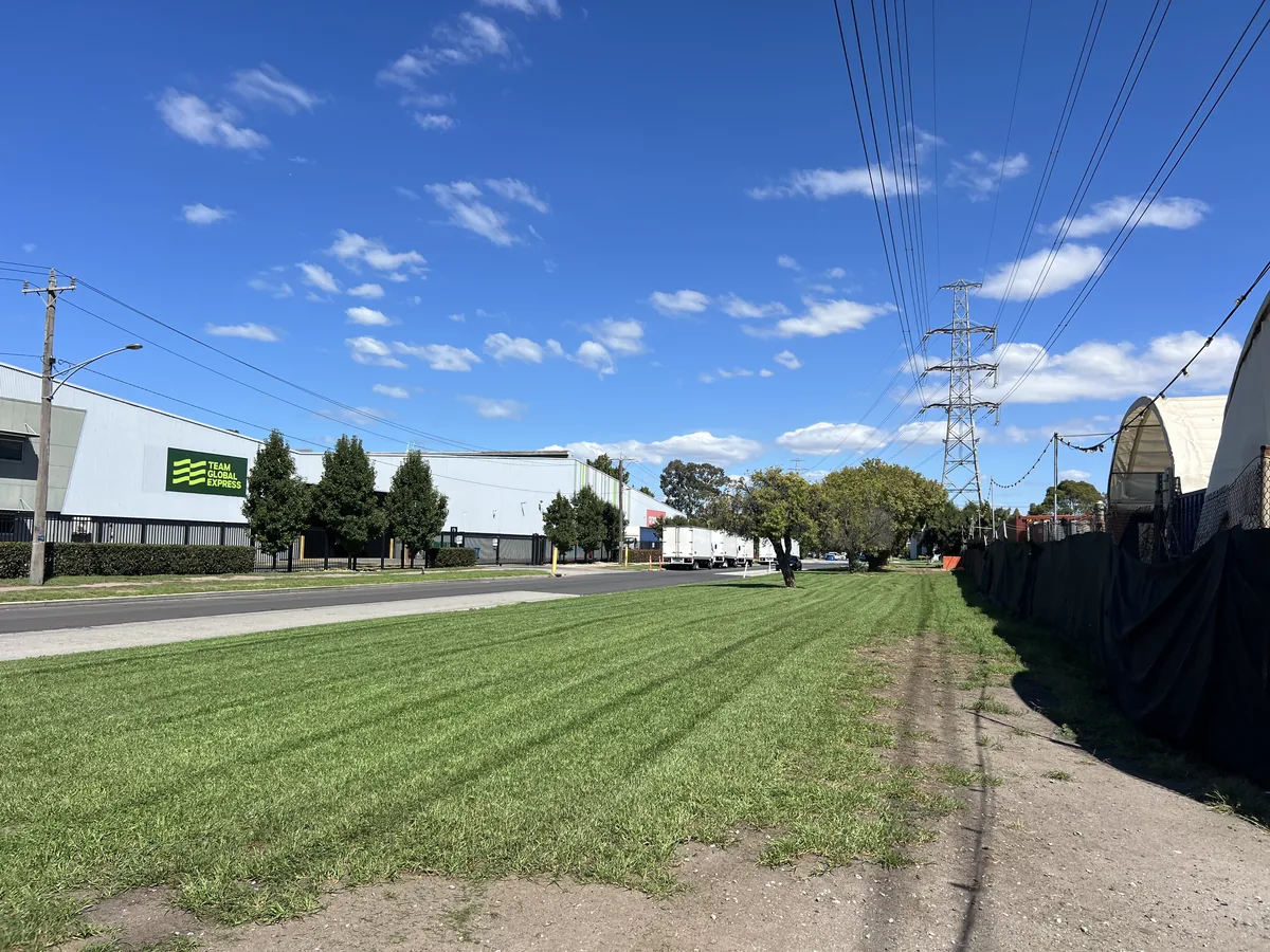 Ride-on mowing a large open block along an industrial frontage